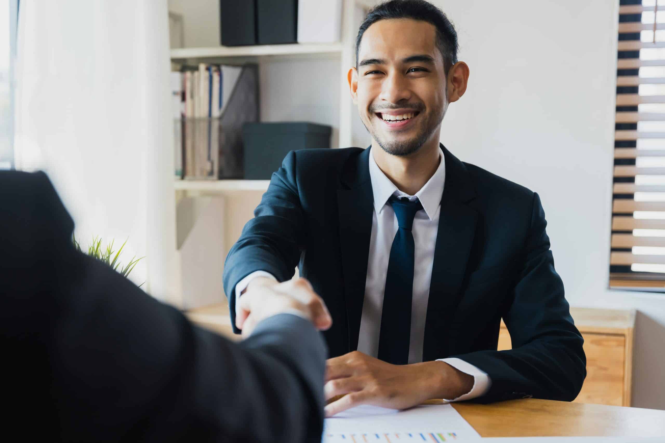 Investor seemingly happy to reach an agreement with an investment manager, about the investor's portfolio. The two parties are in a modern office with a wooden desk.