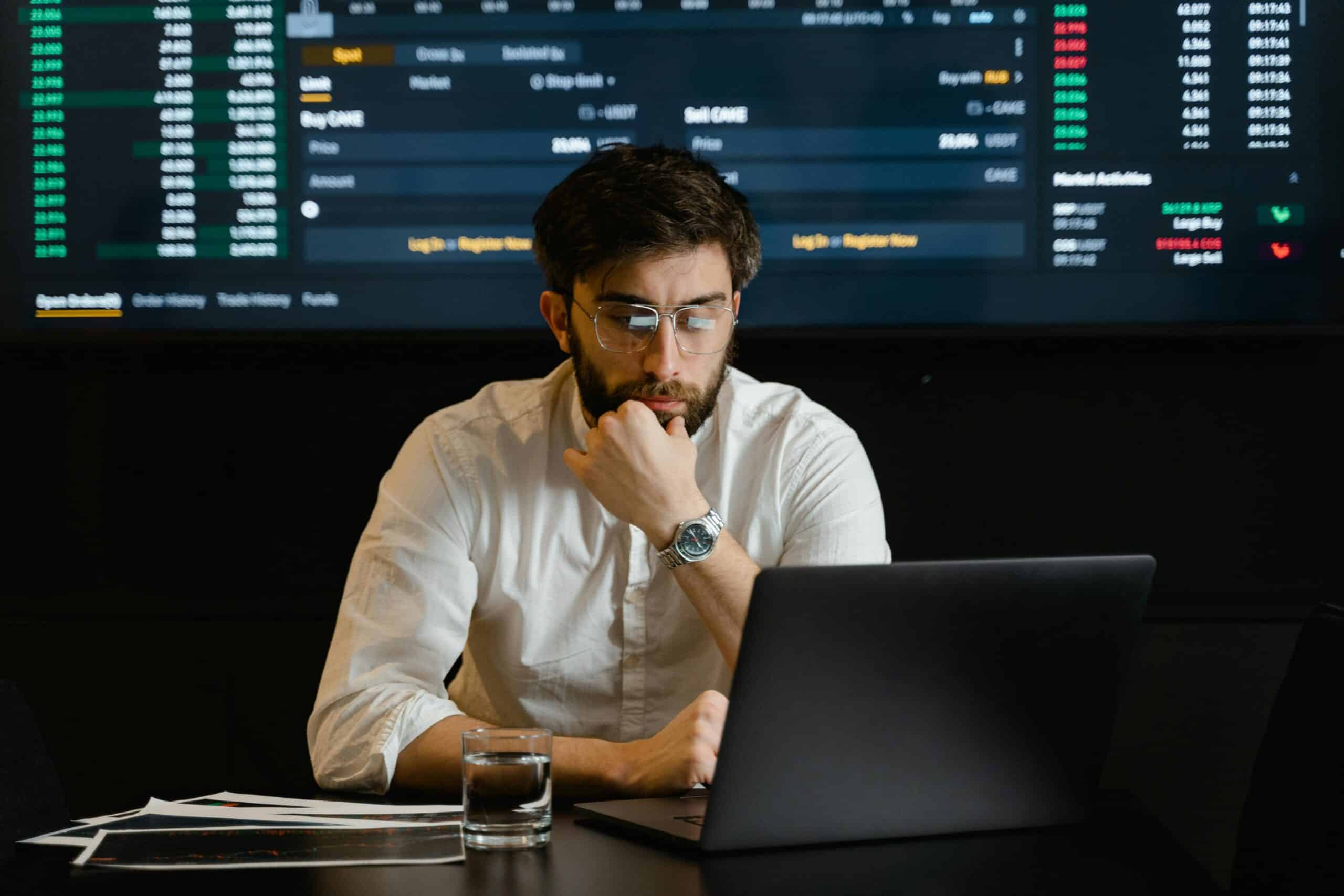 Financial analyst conducting a Source of wealth check in a modern office with bulletin board showing financial stats behind him.